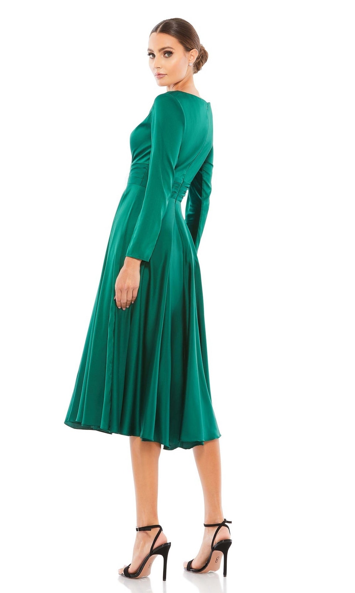 A woman stands, looking over her shoulder in black heels, wearing the elegant Emerald Midi Wedding Guest Dress: Mac Duggal 67527 with long sleeves and a flared skirt. The vibrant green pops against the white background.